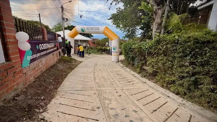 Placa huella de concreto recién construida en un camino rural, con un arco inflable de la Gobernación del Valle al fondo