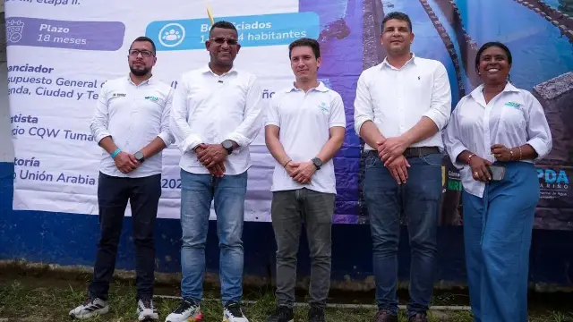 Cinco funcionarios y líderes de pie frente a un pendón con los datos de la obra del acueducto de Tumaco.