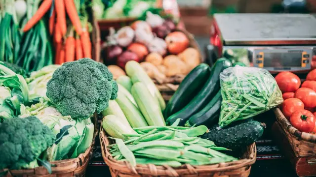 Canastos con brócoli, habichuelas, calabacines, zanahorias y tomates en un puesto de mercado