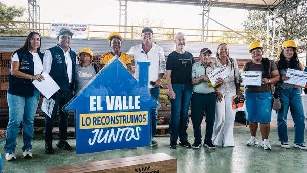 Personas, varias con casco, en un banco de materiales junto a un aviso que dice «El Valle lo reconstruimos juntos».