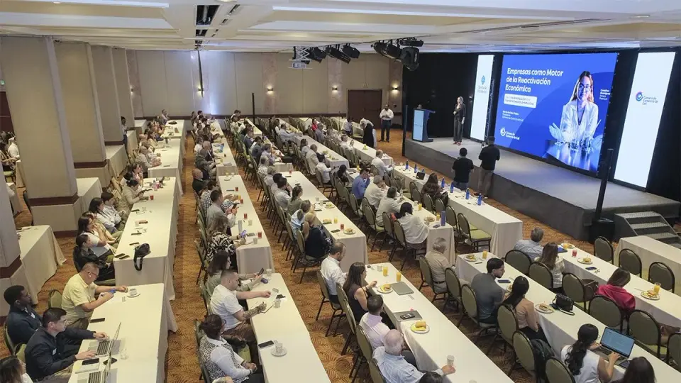 Vista del salón del seminario Perspectivas económicas, con asistentes en mesas largas frente a la tarima y la pantalla