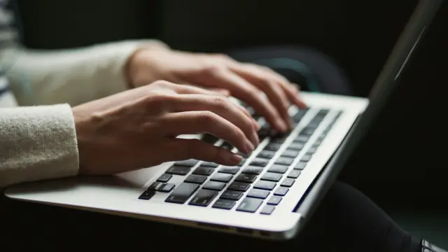 Manos escribiendo en el teclado de un computador portátil