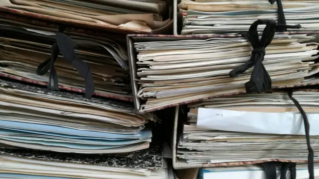 Carpetas de expedientes antiguos atadas con cintas negras y apiladas en un archivo