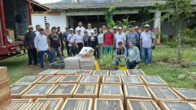 Decenas de cajas de colmenas en el césped frente a un grupo de productores y técnicos de la Gobernación, junto al camión que las trajo