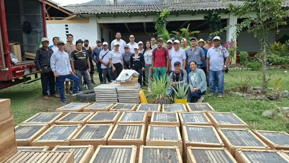 Decenas de cajas de colmenas en el césped frente a un grupo de productores y técnicos de la Gobernación, junto al camión que las trajo