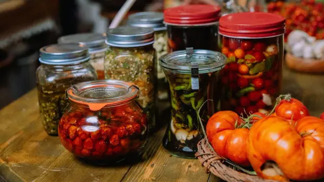 Frascos de conservas caseras sin etiqueta sobre una mesa de madera, junto a tomates