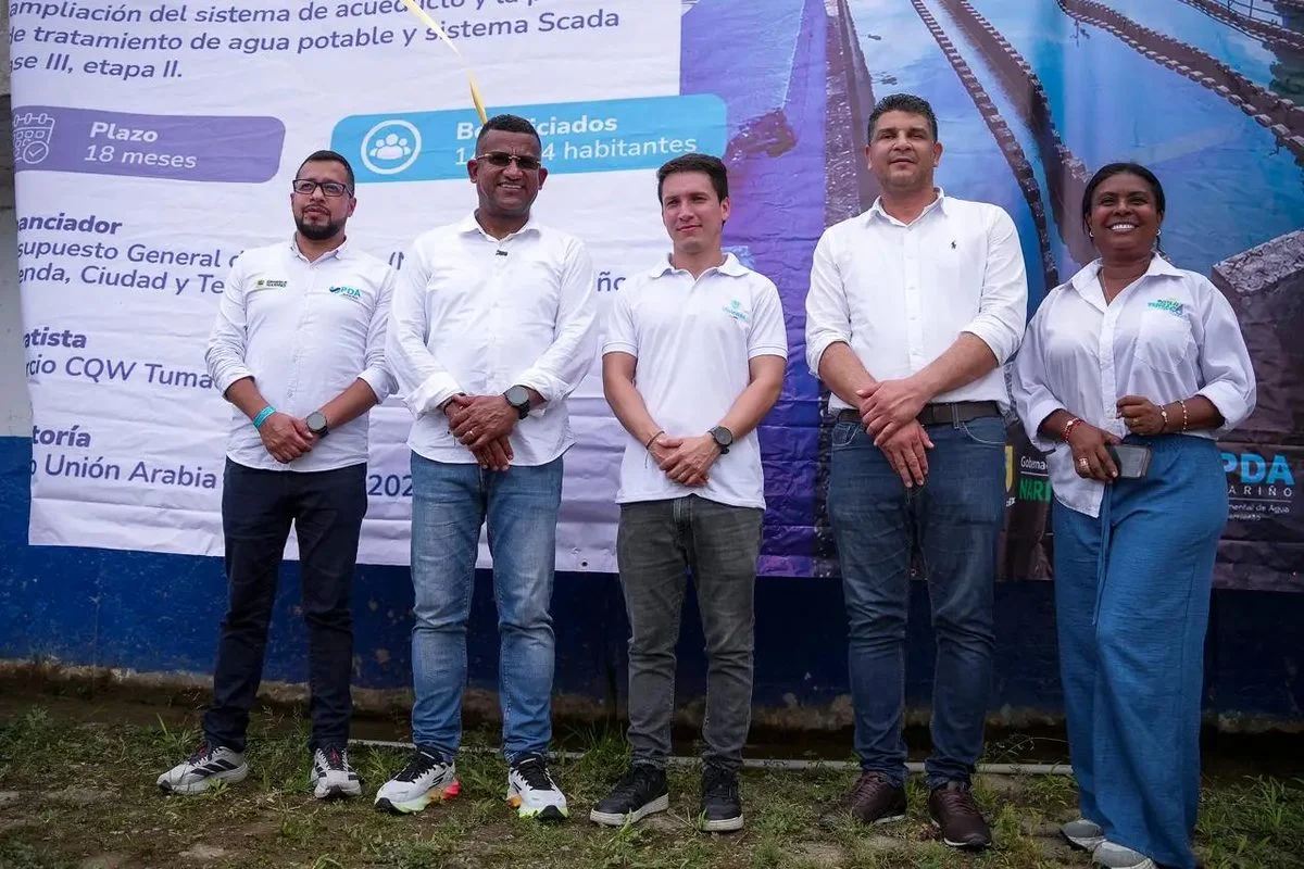Cinco funcionarios posan frente a la valla del proyecto de la planta de tratamiento de agua potable, con plazo de 18 meses