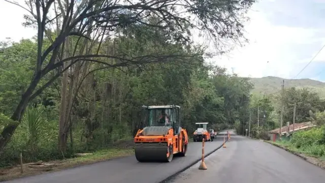 Un compactador de rodillo y una volqueta trabajan sobre el asfalto nuevo de un tramo de la Vía Panorama, entre árboles