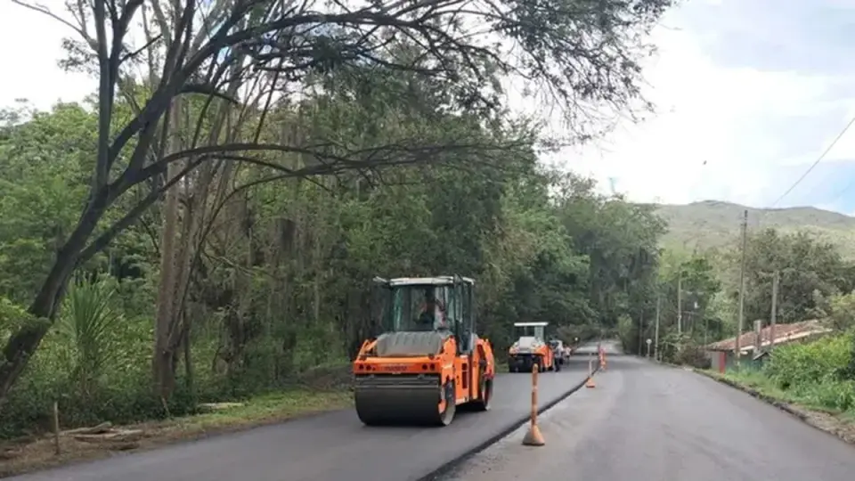 Un compactador de rodillo y una volqueta trabajan sobre el asfalto nuevo de un tramo de la Vía Panorama, entre árboles