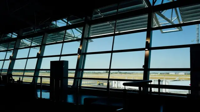 Ventanales de una sala de abordaje con vista a la pista de un aeropuerto en un día despejado