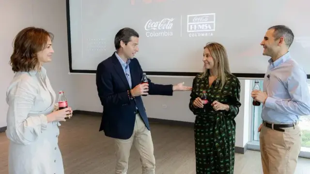 El ministro de Comercio, Mauricio Gómez Amín, conversa con tres asistentes, botellas de gaseosa en mano, frente a una pantalla con los logos de Coca-Cola Colombia y Coca-Cola FEMSA
