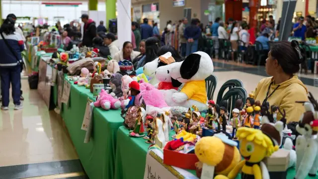 Mesas de emprendimientos con muñecos de peluche y figuras artesanales en el pasillo de un centro comercial de Ipiales, con visitantes al fondo