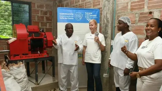 Integrantes de Saca Curachón con traje blanco junto a un trapiche eléctrico rojo en su planta de Buenaventura