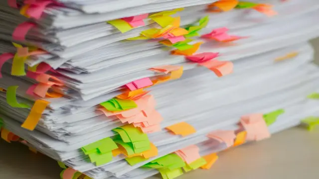 Pila de documentos marcados con notas adhesivas de colores sobre un escritorio
