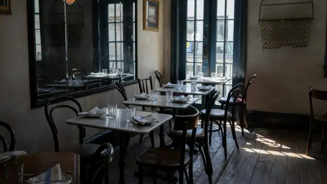 Mesas servidas y sillas vacías en un restaurante pequeño con luz de ventana