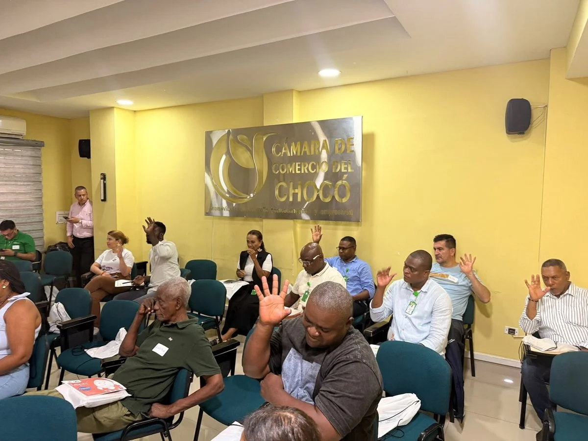 Asistentes levantan la mano durante el taller de educación financiera en un salón de la Cámara de Comercio del Chocó