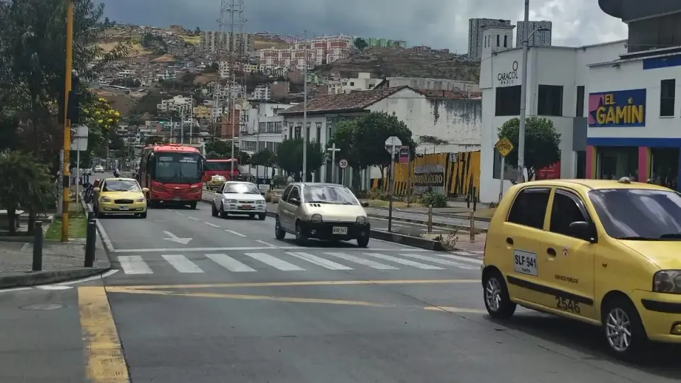 Taxis, carros particulares y un bus urbano circulan por una avenida de Pasto con las laderas de la ciudad al fondo