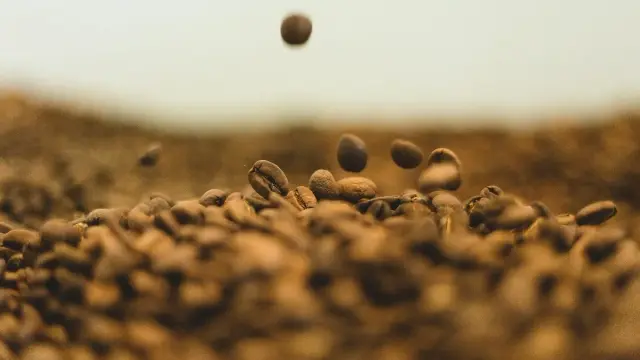 Granos de café tostado cayendo sobre un montón de café
