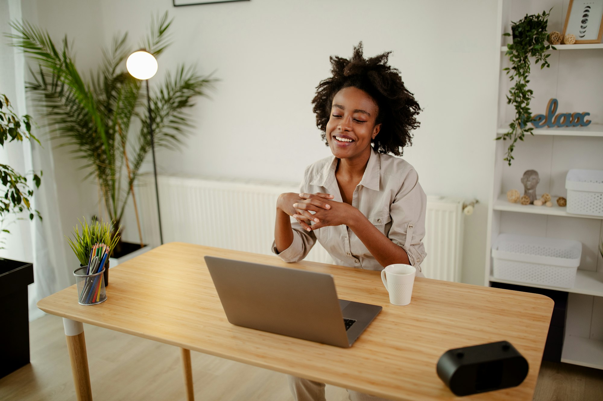 Black smiling businesswoman using laptop, drinking a coffee and having conference call from home.
